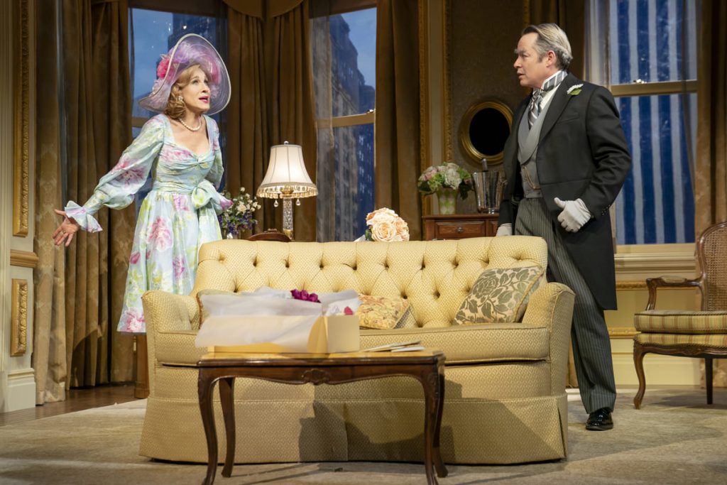 Plaza Suite on stage shot. SJP is dressed in a floral blue dress and also wears a large wedding hat. To her right is Matthew Broderick wearing a three-piece suit. They are having a worried, animated conversation inside a decadent hotel room